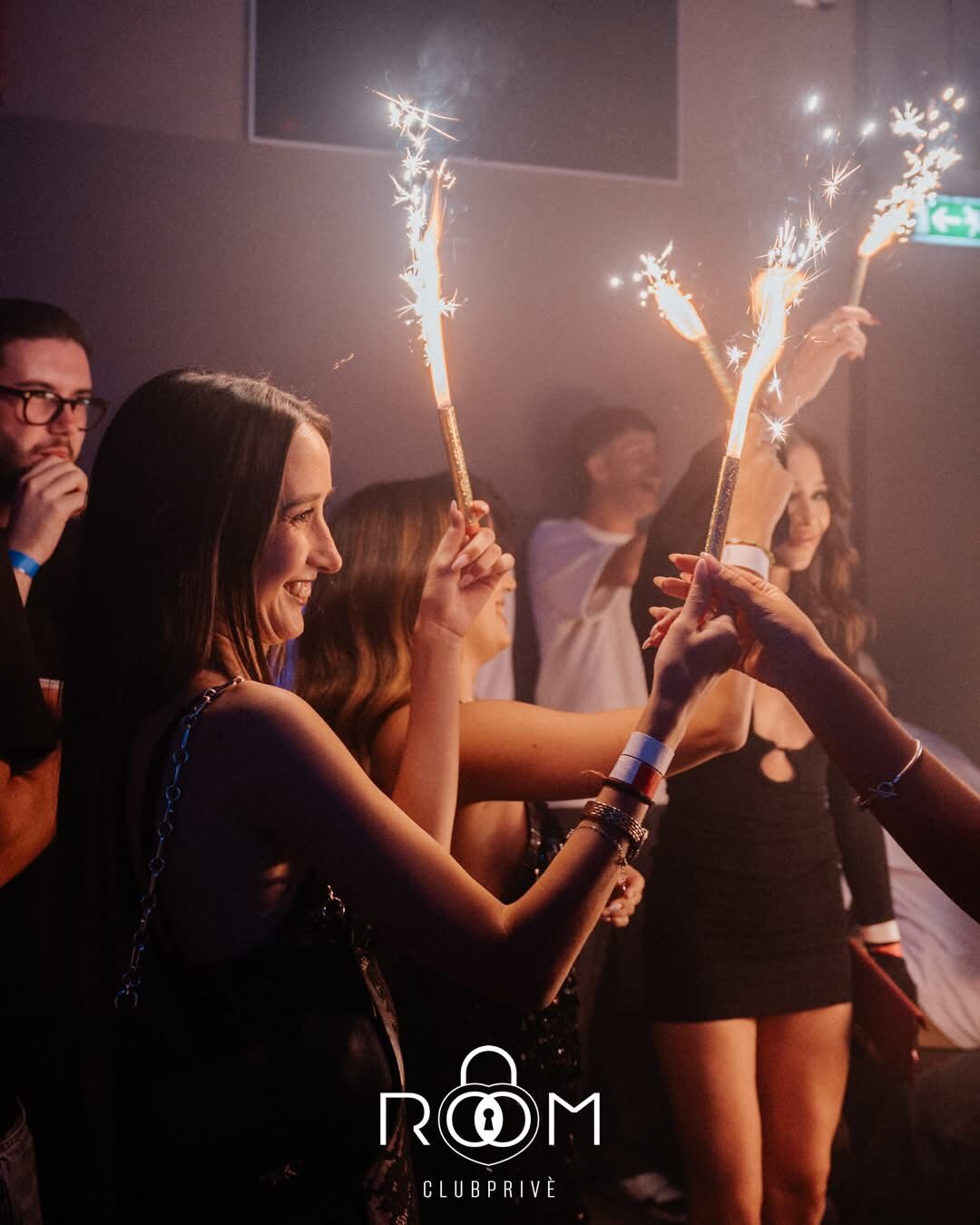 Un gruppo di amiche brinda sorridendo con bottiglie di stelle filanti scintillanti in pista.
